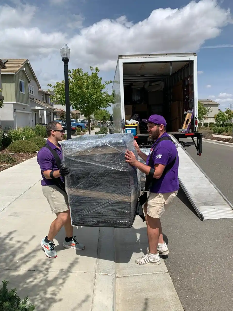 Two movers carrying wrapped furniture up the truck ramp